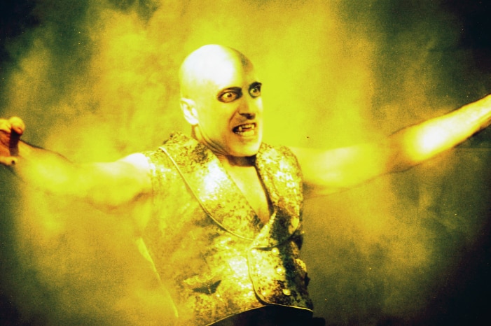 A male actor on stage dressed as Dracula, with yellow light around him.
