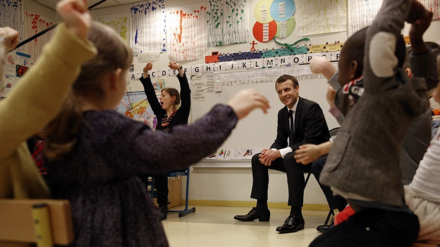 French President Emmanuel Macron listens to pre-school children.
