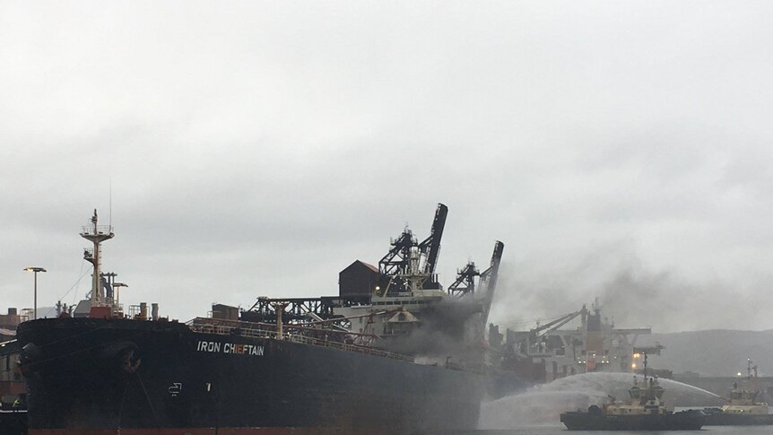 Firefighters hose water onto the Iron Chieftain as it is docked in Port Kembla.