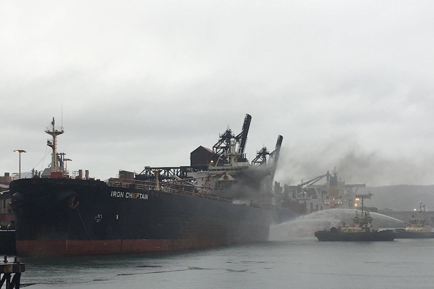 Firefighters hose water onto the Iron Chieftain as it is docked in Port Kembla.