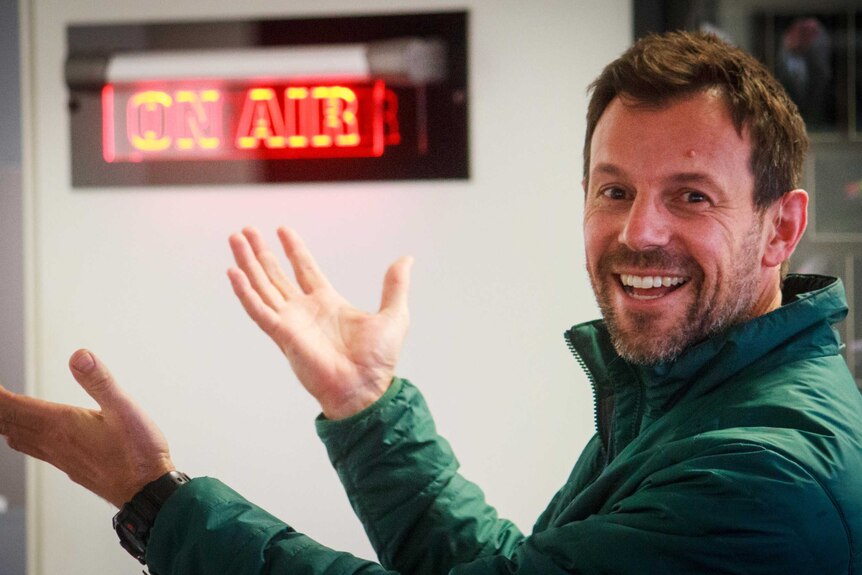 A man in radio studio with his hands raised smiling at the camera, someone who found job satisfaction after a career change.