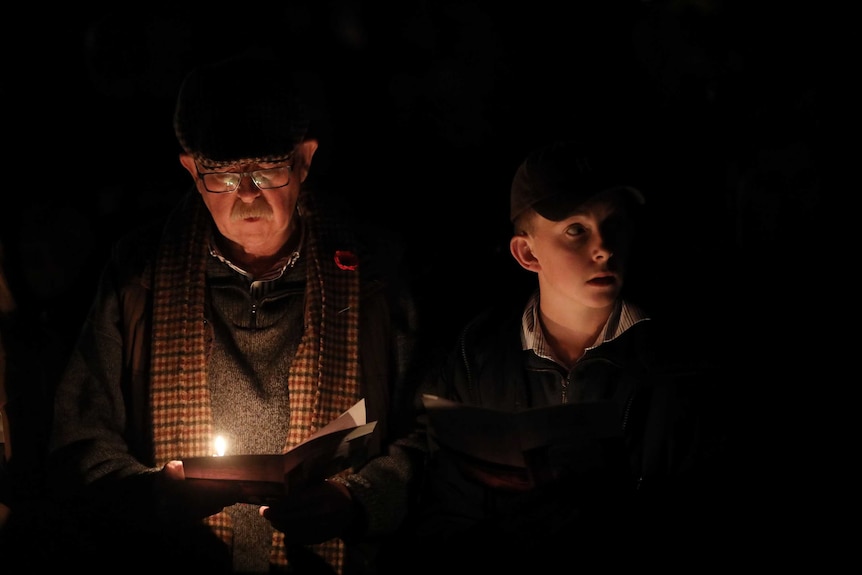 An older man and a young boy at the Anzac Day dawn service read by torch light.