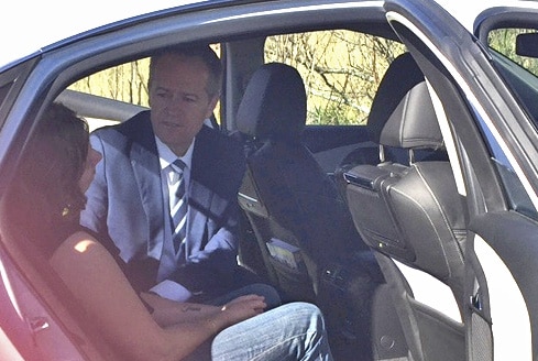 Bill Shorten sitting in a car, talking to a woman.