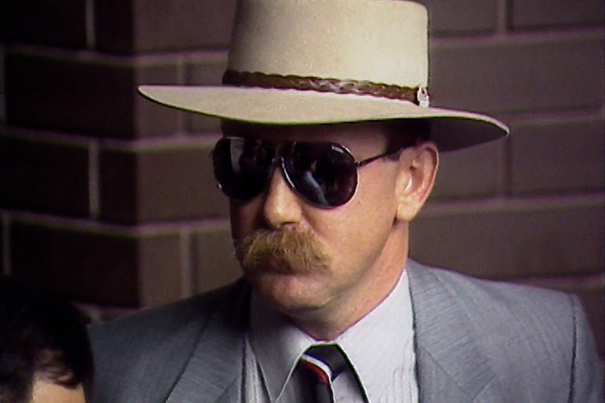A man with a moustache wearing aviators and a wide brimmed hat.