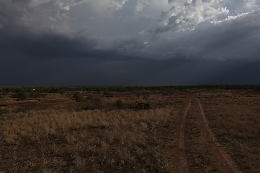 dirt tracks move away from us as dark clouds sit over top covering the red earth