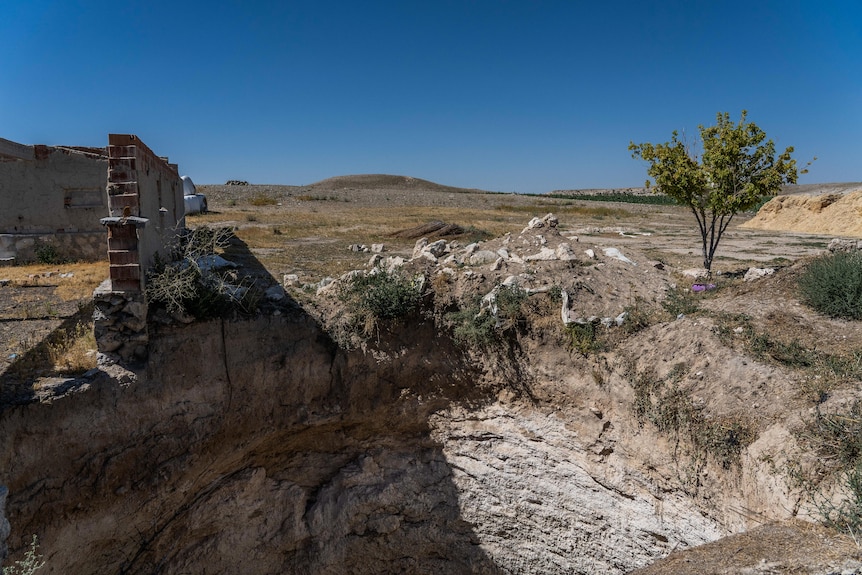 A large sinkhole is seen next to a crumbling structure on a wide open landscape