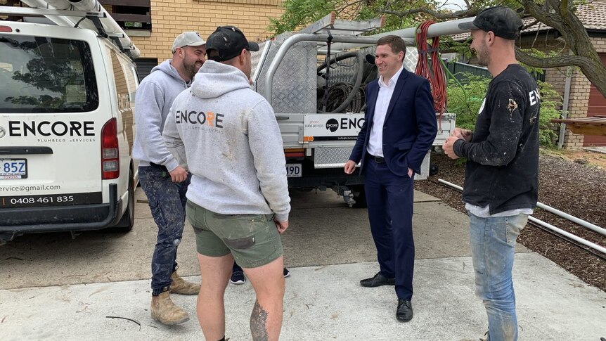 Three tradies, all men, stand next to Liberal leader Alastair Coe who is laughing