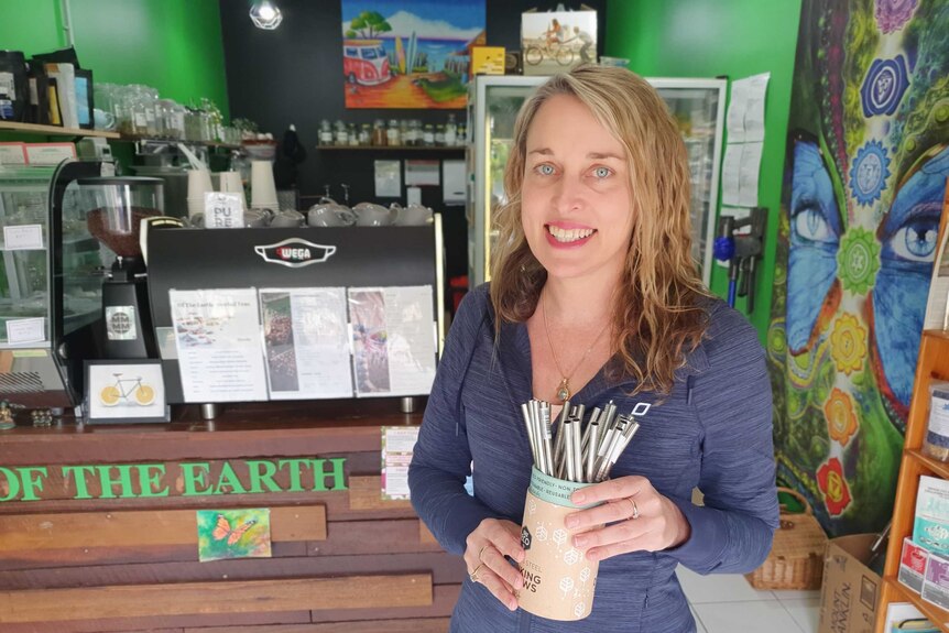 A woman in a cafe holding a jar full of stainless steel straws.