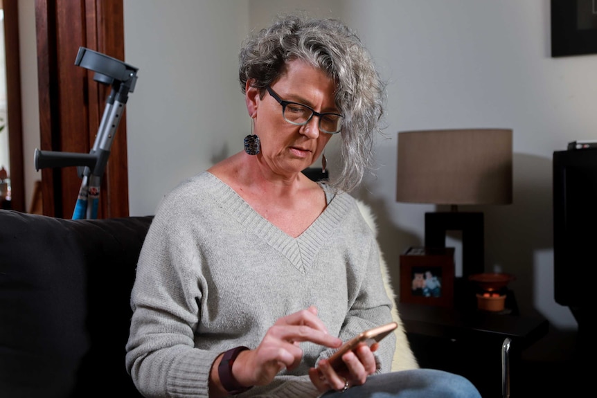 Woman with grey hair and a grey jumper looks at phone in her hand.