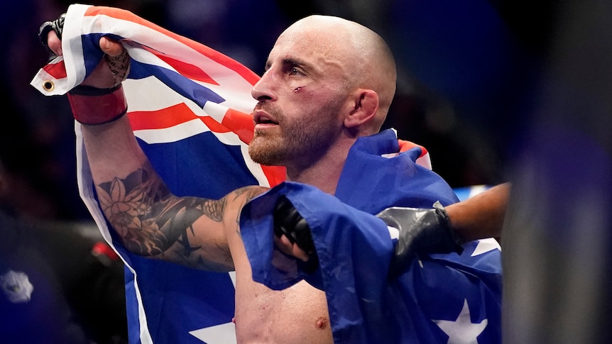 Alexander Volkanovski has cuts on his face as he drapes an Australian flag over his shoulders