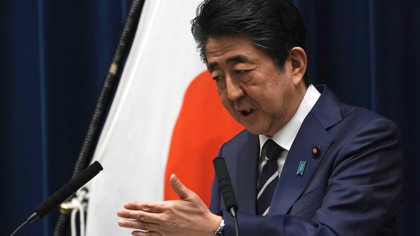 Japanese Prime Minister Shinzo Abe gestures as he speaks from a podium.