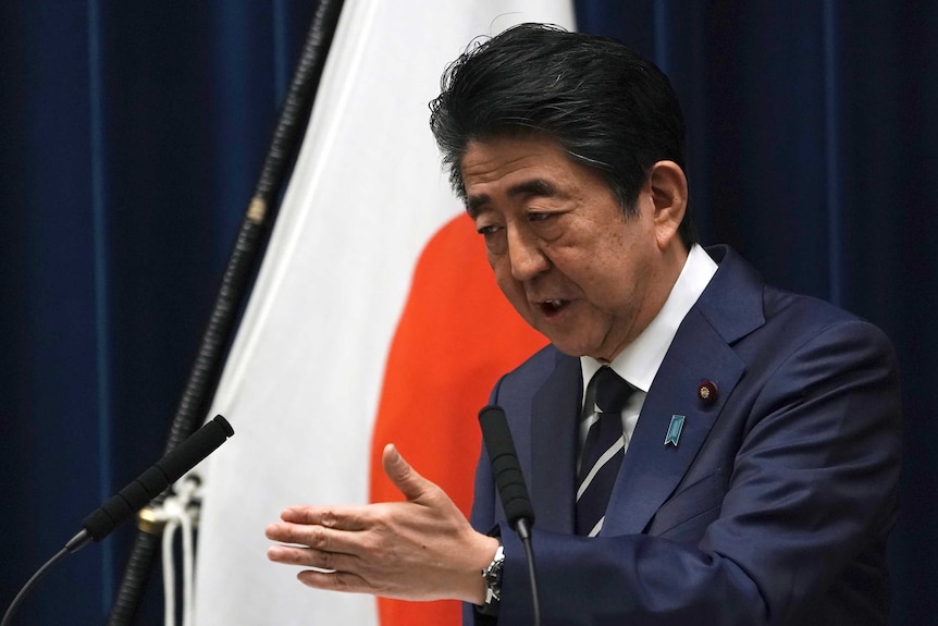 Japanese Prime Minister Shinzo Abe gestures as he speaks from a podium.