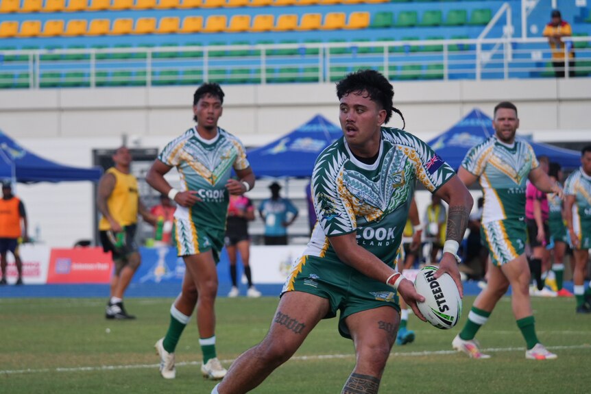 A Cook Islands player runs with the ball on the field, about to pass.