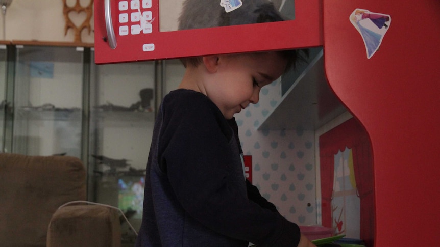 A young boy pretends to 'make eggs' on a plastic stove in his play kitchen.