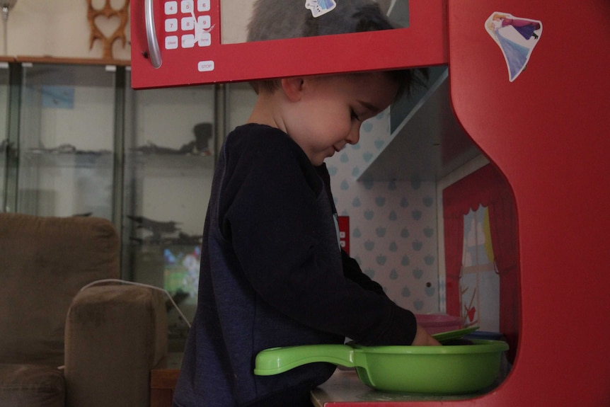 A young boy pretends to 'make eggs' on a plastic stove in his play kitchen.