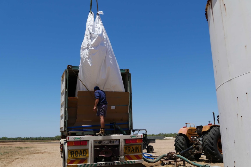 Person unloads large white bag full of molasses from shipping container