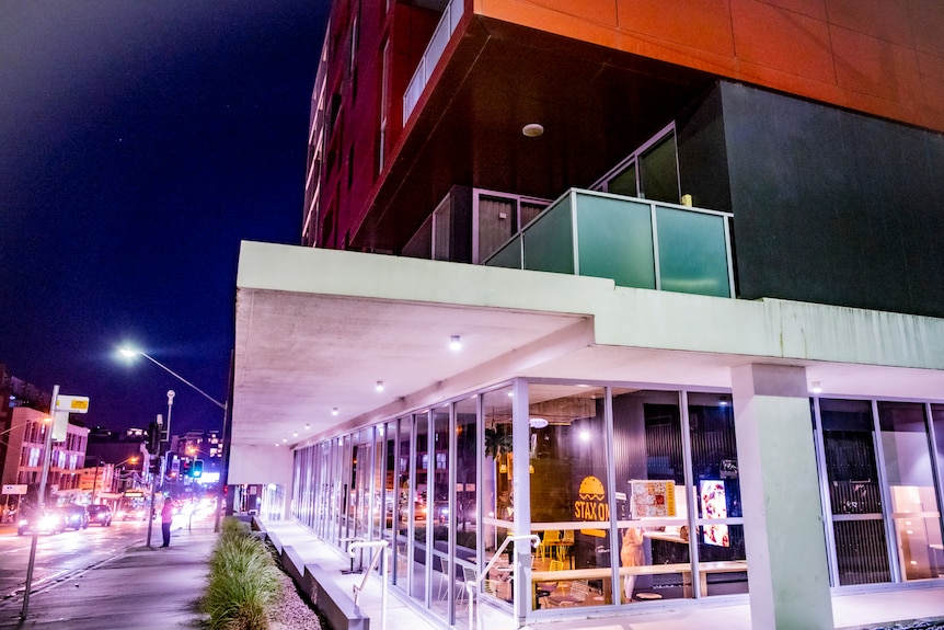 A night shot of a modern apartment block with a burger store at the bottom level