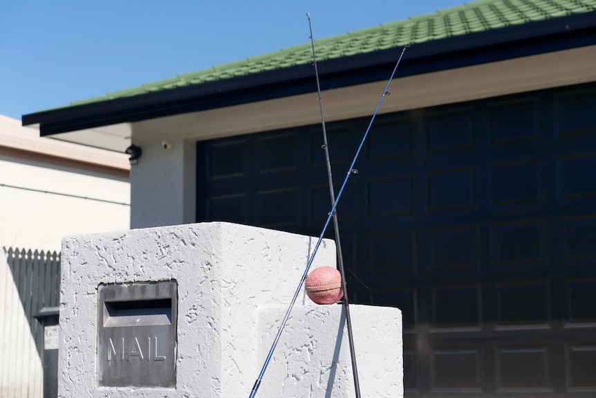 Two fishing rods, crossed with cricket ball in between, out the front of a house.