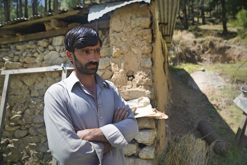 A man stands in front of his house with his arms crossed