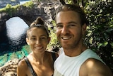 Jolie King and Mark Firkin take a selfie together with water and cliffs in the background.