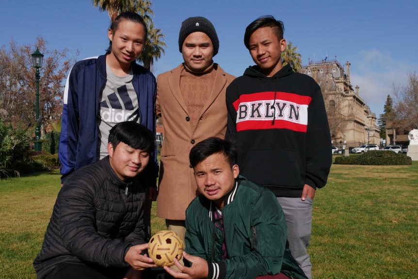 Five men stand in a park holding a small yellow ball.