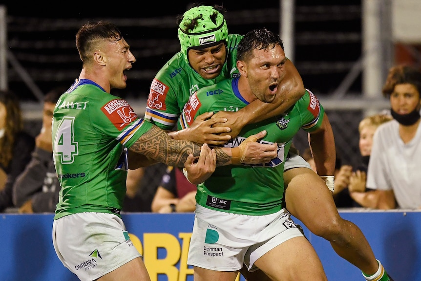 Three Canberra Raiders NRL players embrace as they celebrate a try against the Warriors.