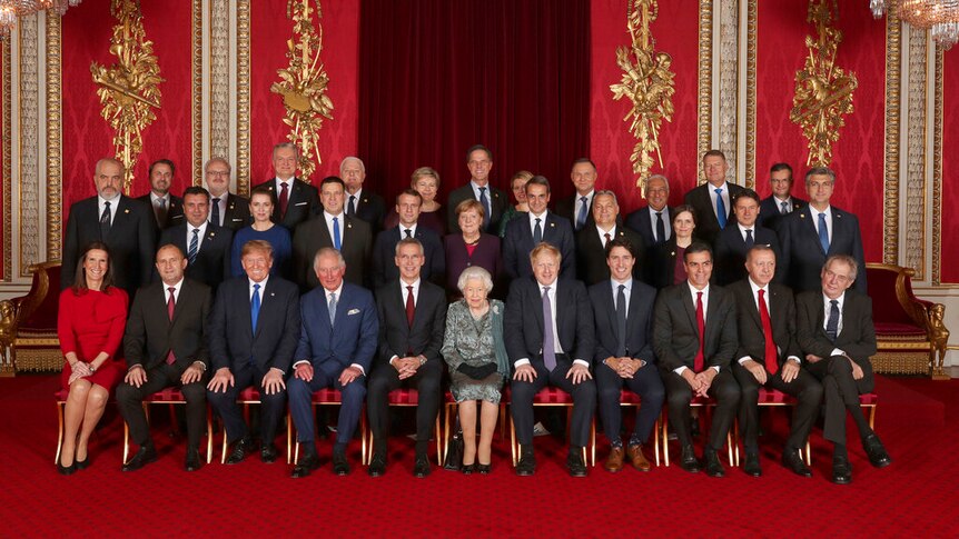 Distinguished world leaders sit and stand in lines for a large group photo in a luxuriously decorated room