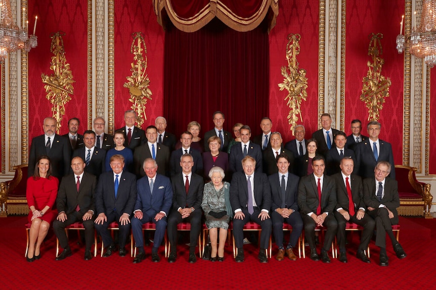 Distinguished world leaders sit and stand in lines for a large group photo in a luxuriously decorated room
