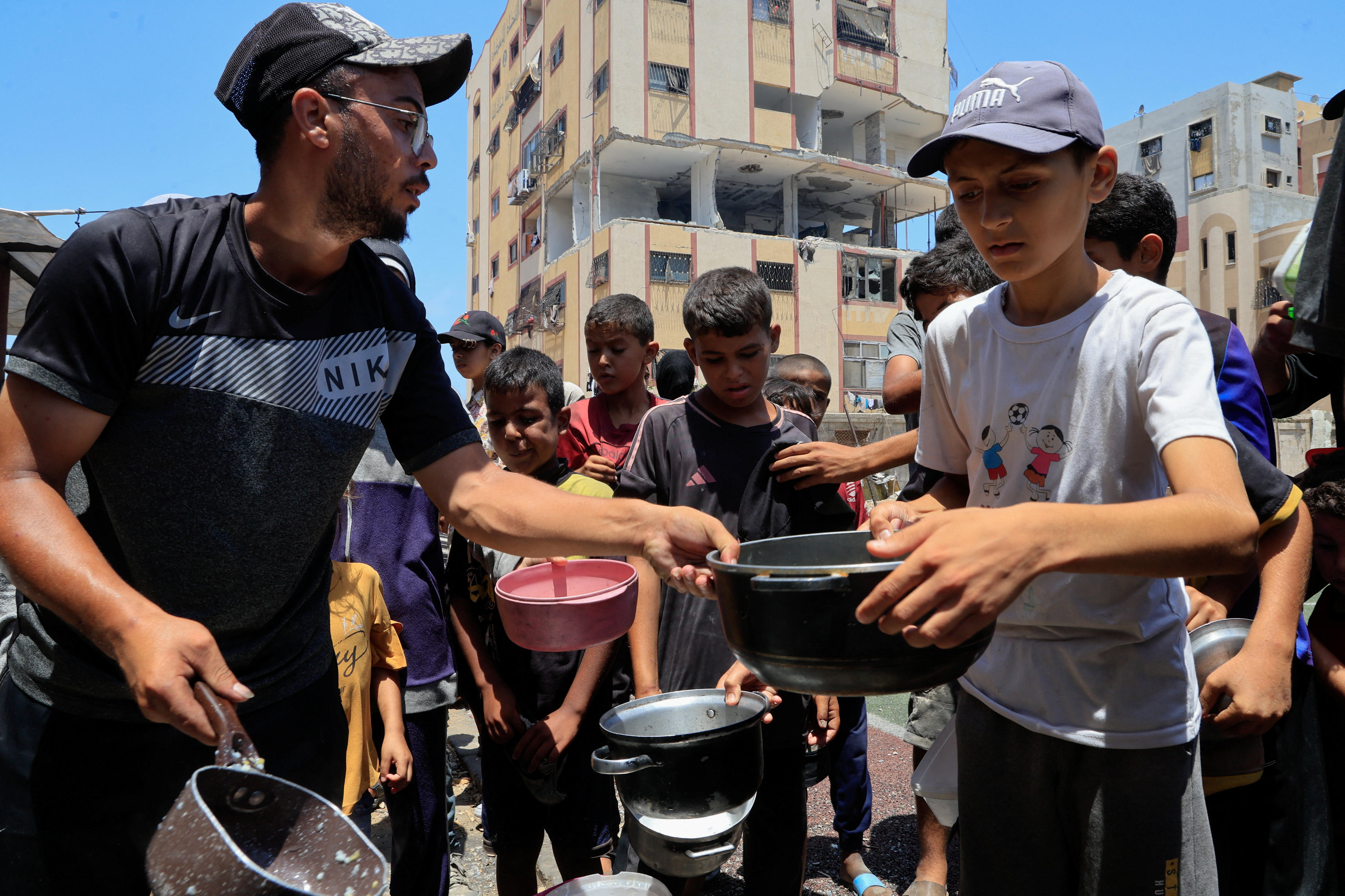A line of young children lining up with bowls at a charity kitchen.