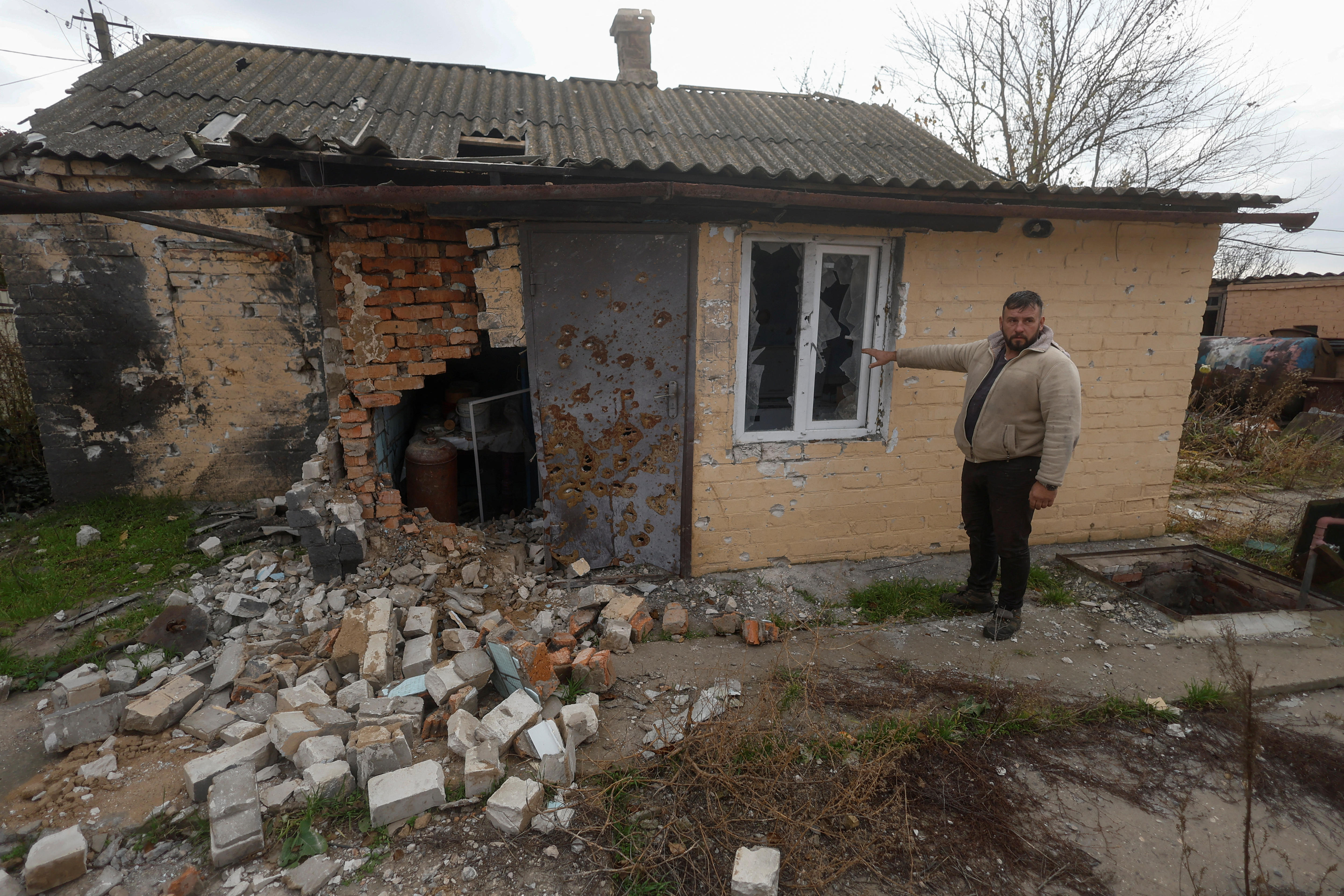 A man points to the crumbling wall of a house damaged by military strikes.
