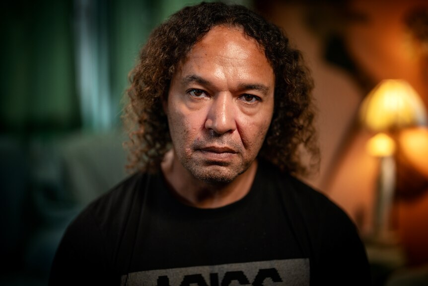 Man wearing a dark shirt with medium curly brown hair, looking serious.