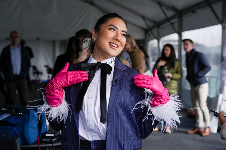 A woman in a suit with pink feathered gloves on