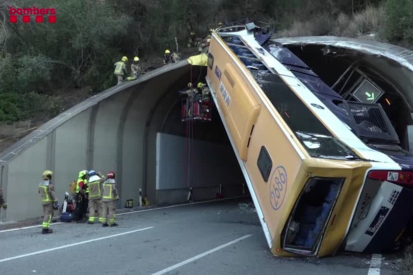 A bus is nearly upside down at the exit of a tunnel with firefighters working to stabilise it and get people out of it