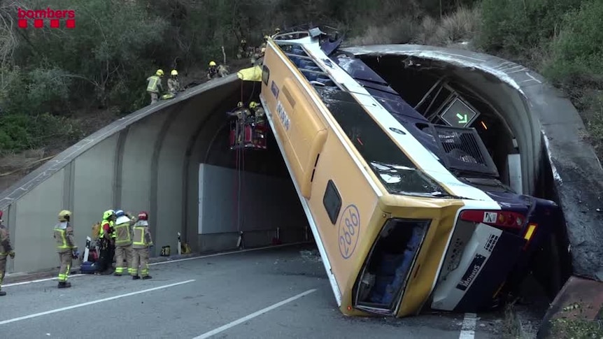 A bus is nearly upside down at the exit of a tunnel with firefighters working to stabilise it and get people out of it