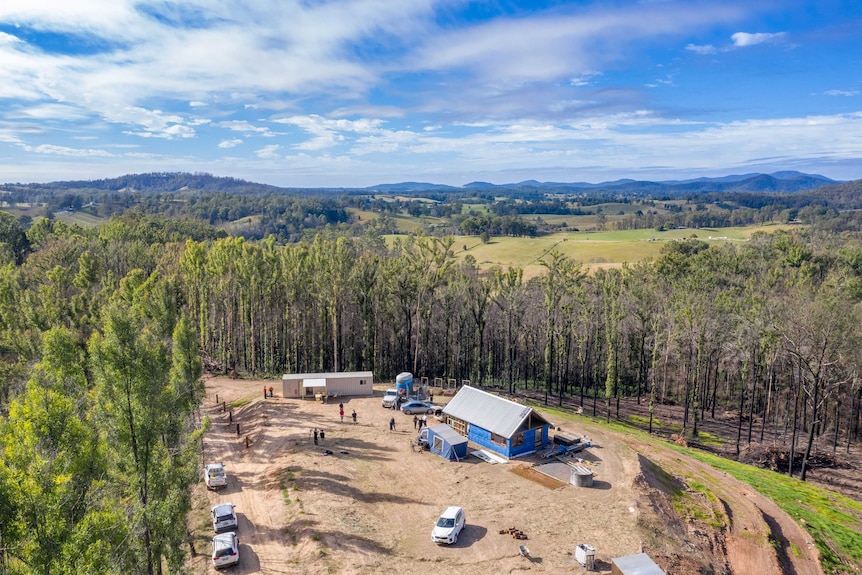Tradesmen at a house being built in a clearing on a  property at Nambucca, surrounded by trees and paddocks, with a blue sky