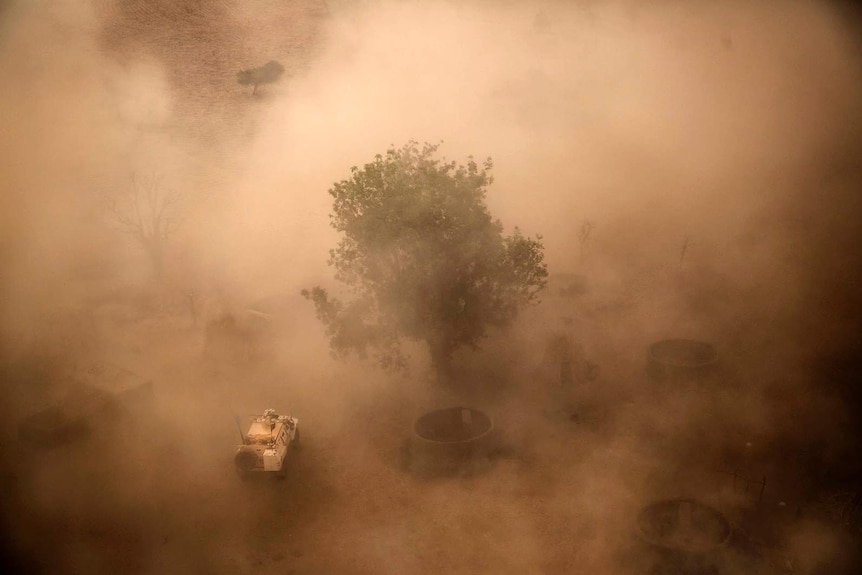 An aerial shot showing a UN vehicle through past red dust and smoke.