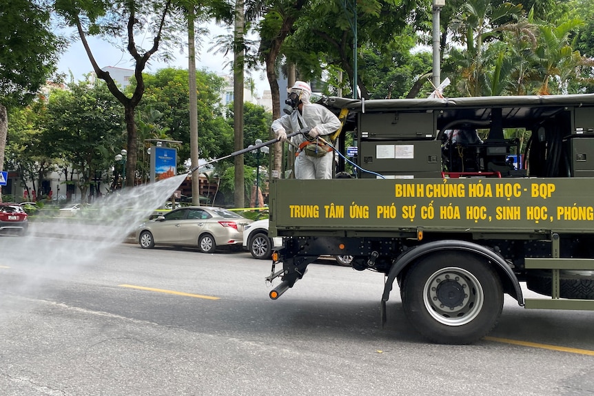 Military personnel wearing PPE spray disinfectant on the streets during a lockdown in Hanoi