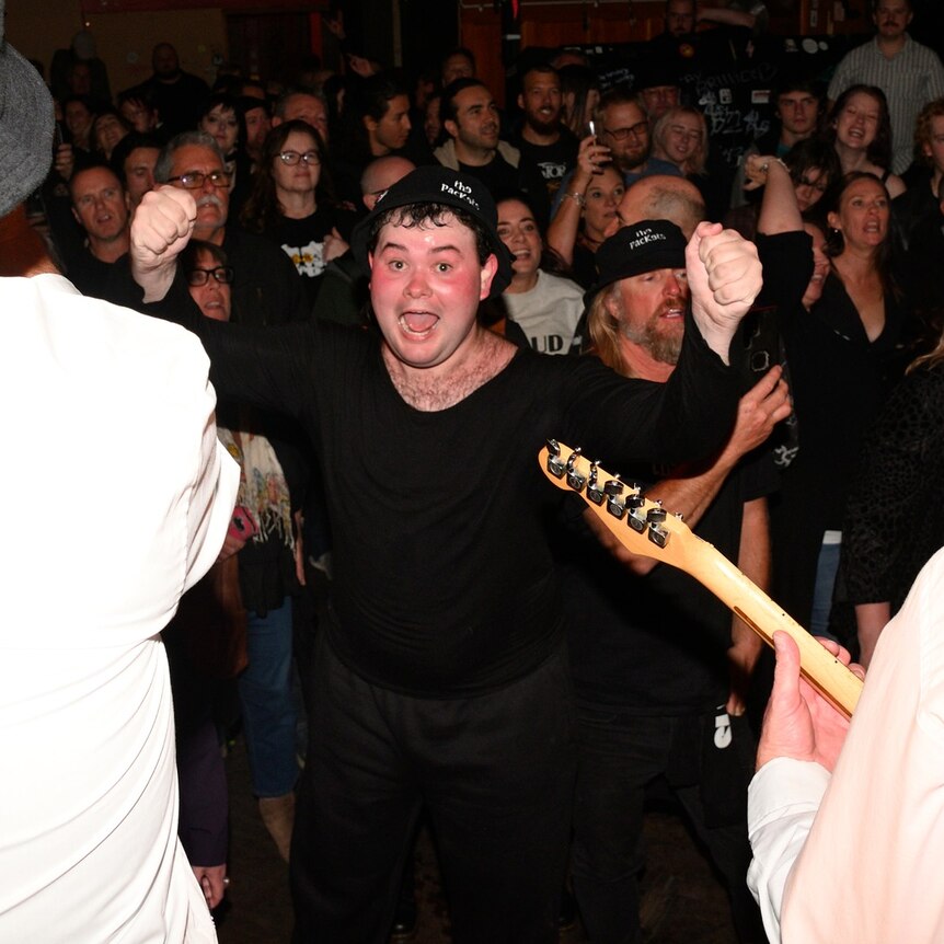 man cheering in a crowd at live music event, back of performers seen in foreground