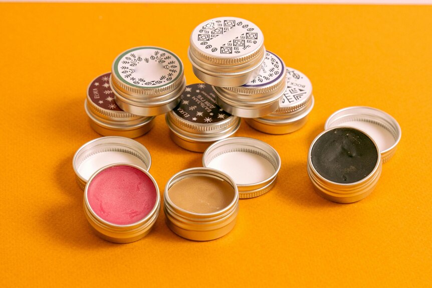 Lip balm containers piled up on orange background. 
