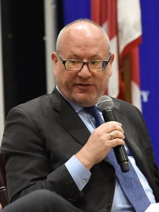 A man wearing a suit and tie speaks into a microphone.