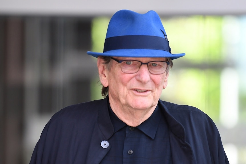 man in coat, blue hat and glasses walking towards camera