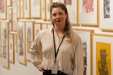 A smiling, fair-haired woman stands in an art gallery.
