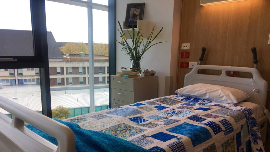 A hospital bed with a blue patchwork quilt