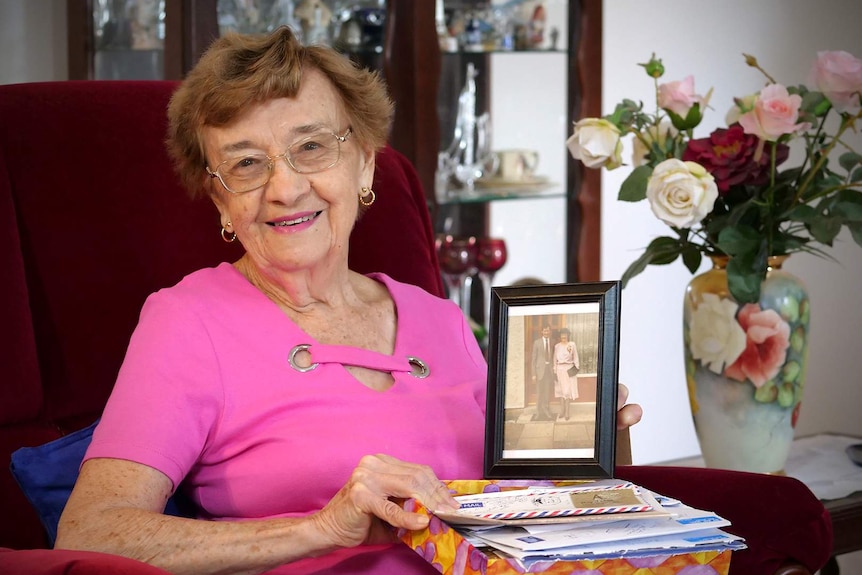 Jill Stretton sits in her loungeroom holding a box of letters on her lap, she holds a photo of her pen pal of 70 years, Cathie.