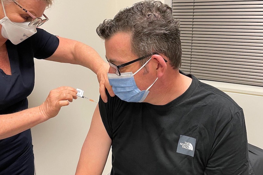 Victorian Premier Daniel Andrews, wearing a face mask, receives a vaccine from a nurse in a face mask.