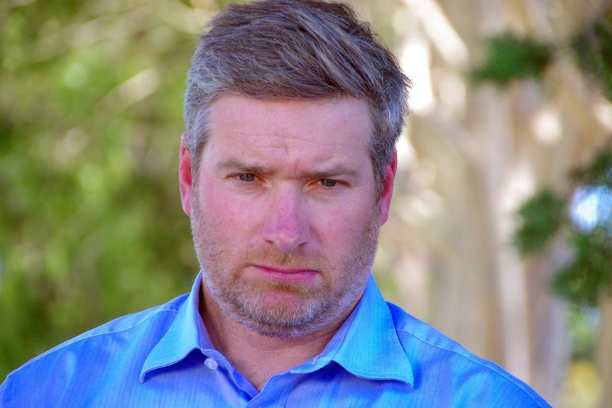 Brendon Grylls looking solemn with green trees in the background.