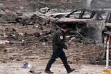 Police officer walks by charred cars and trees on street.