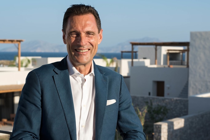 Peter Fankhauser stands on an outdoor balcony, looking off to the distance. He is wearing a suit.