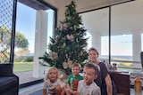 Three children and their mother sit in front of a Christmas tree