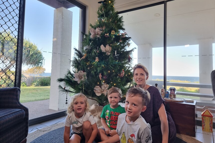 Three children and their mother sit in front of a Christmas tree